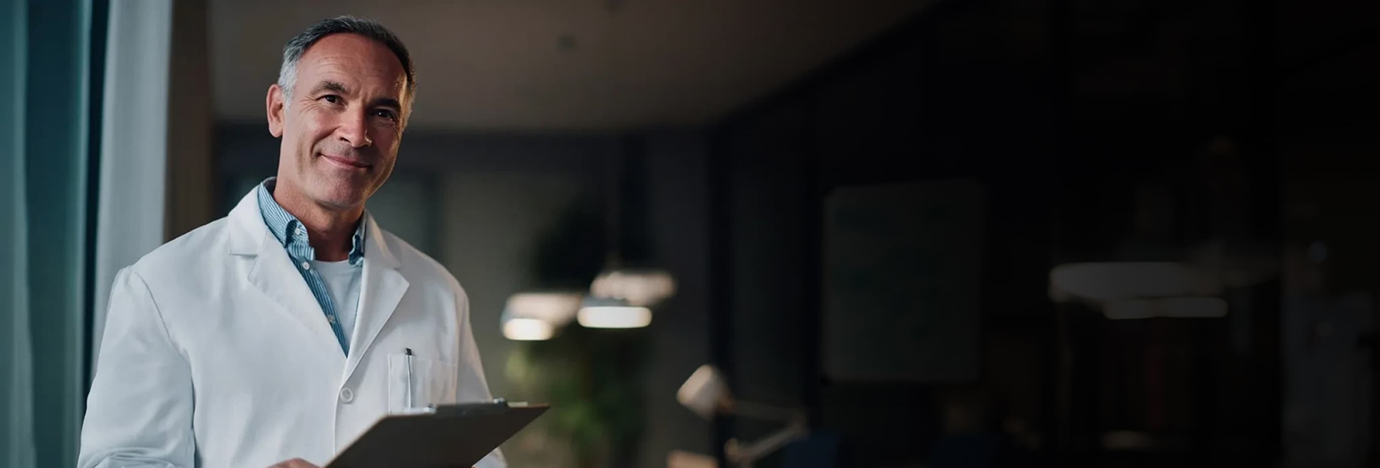 Médico de jaleco usando tablet em ambiente interno iluminado.