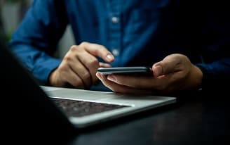 Pessoa usando smartphone com computador à frente