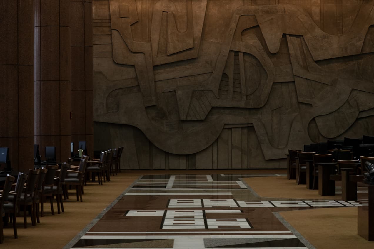 Salão amplo com cadeiras alinhadas e parede de concreto com formas geométricas.