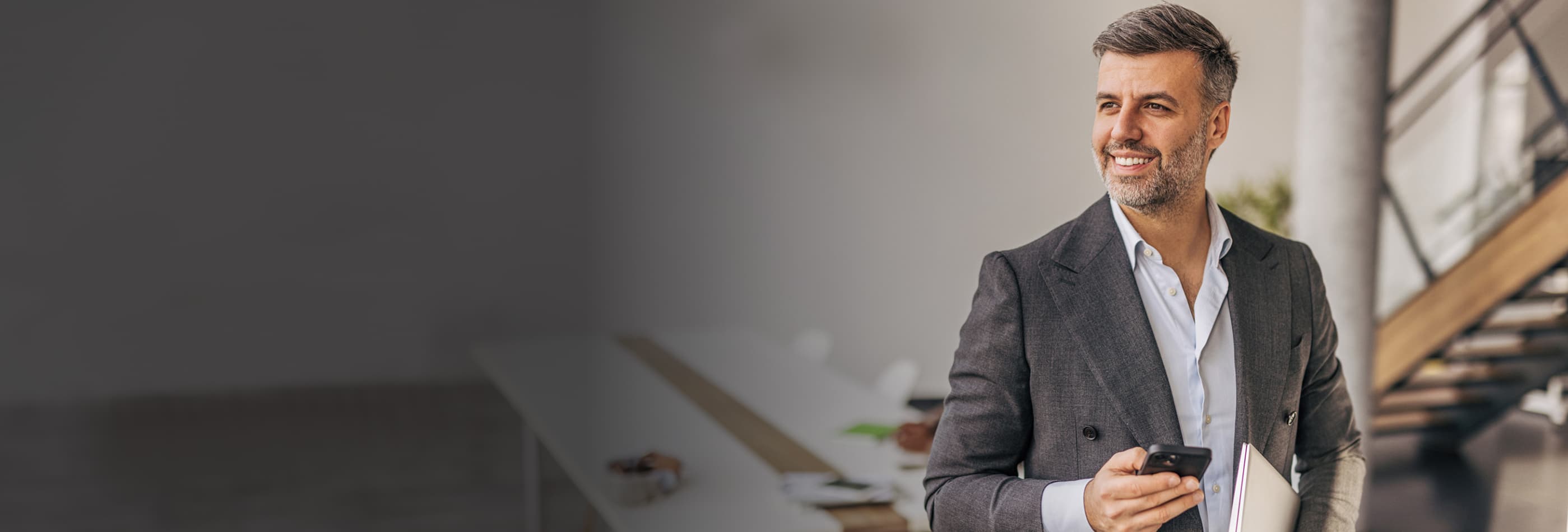 Homem de terno azul analisando informações no tablet em um escritório com vista para a cidade